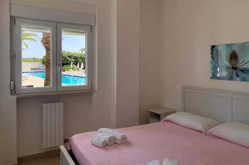 Une chambre lumineuse avec un lit recouvert d'une couverture rose et une vue sur une piscine.