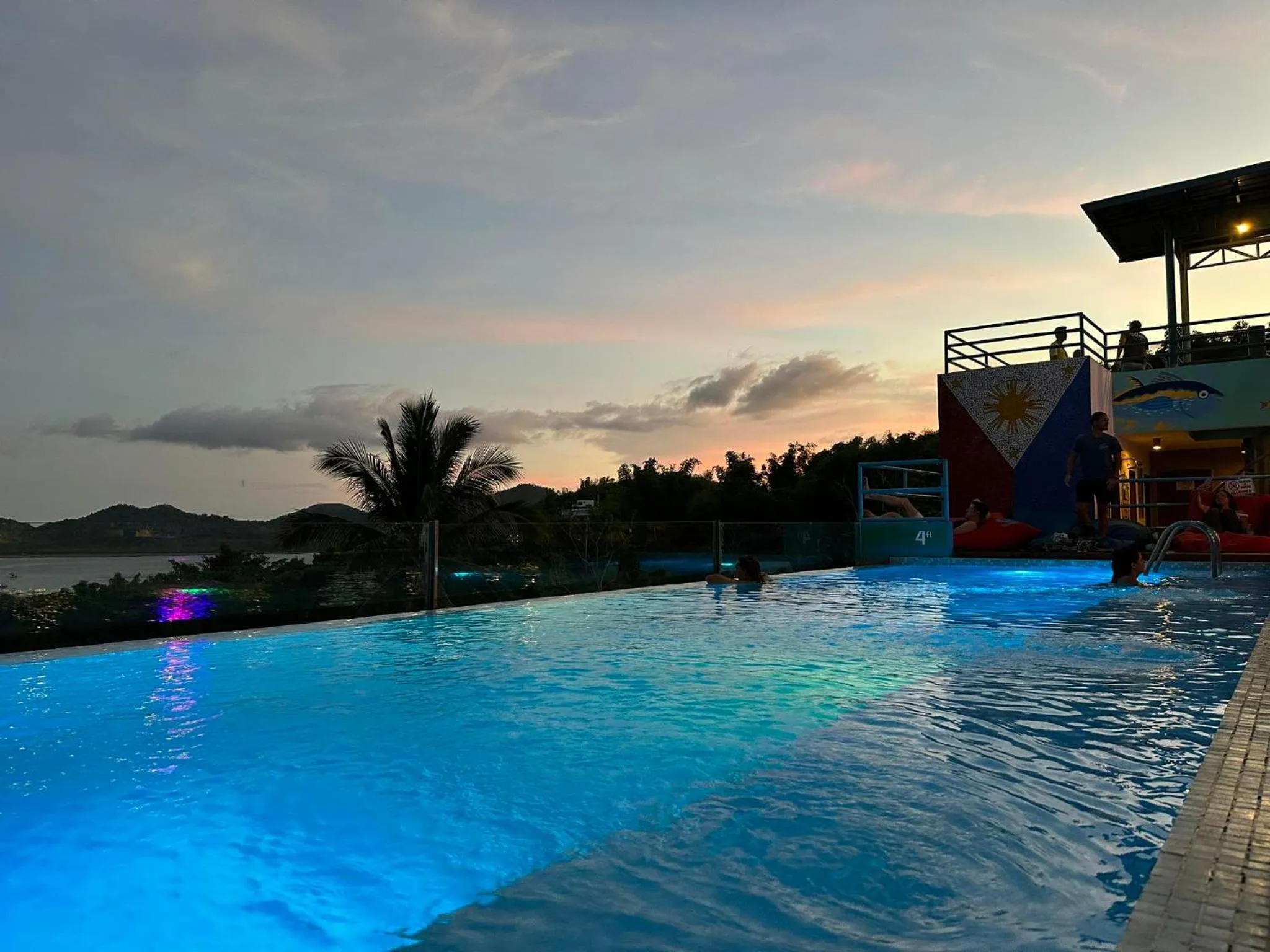 Piscine à débordement illuminée avec vue sur la mer au coucher du soleil.