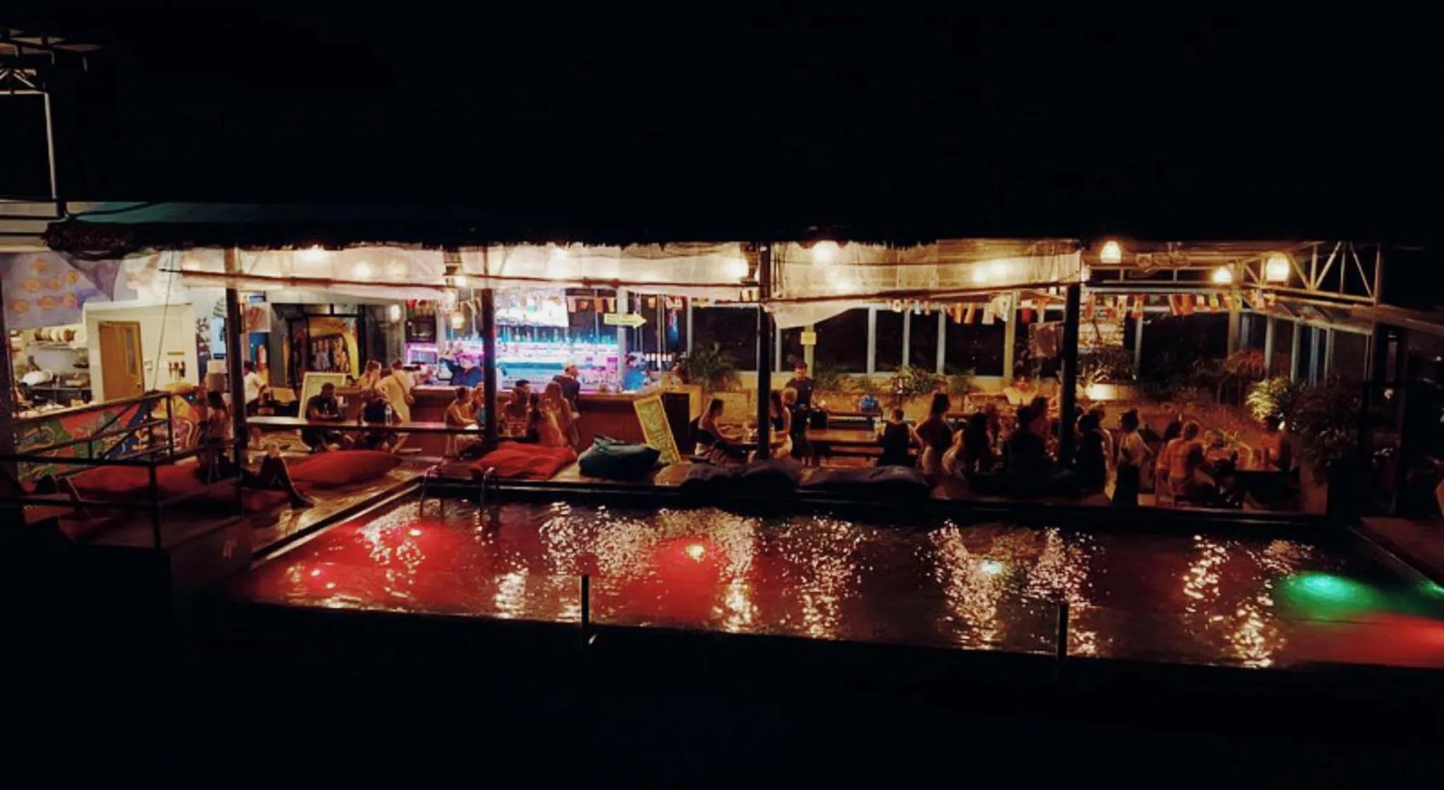 Espace de restauration en extérieur illuminé avec des tables et des chaises près d'une piscine.