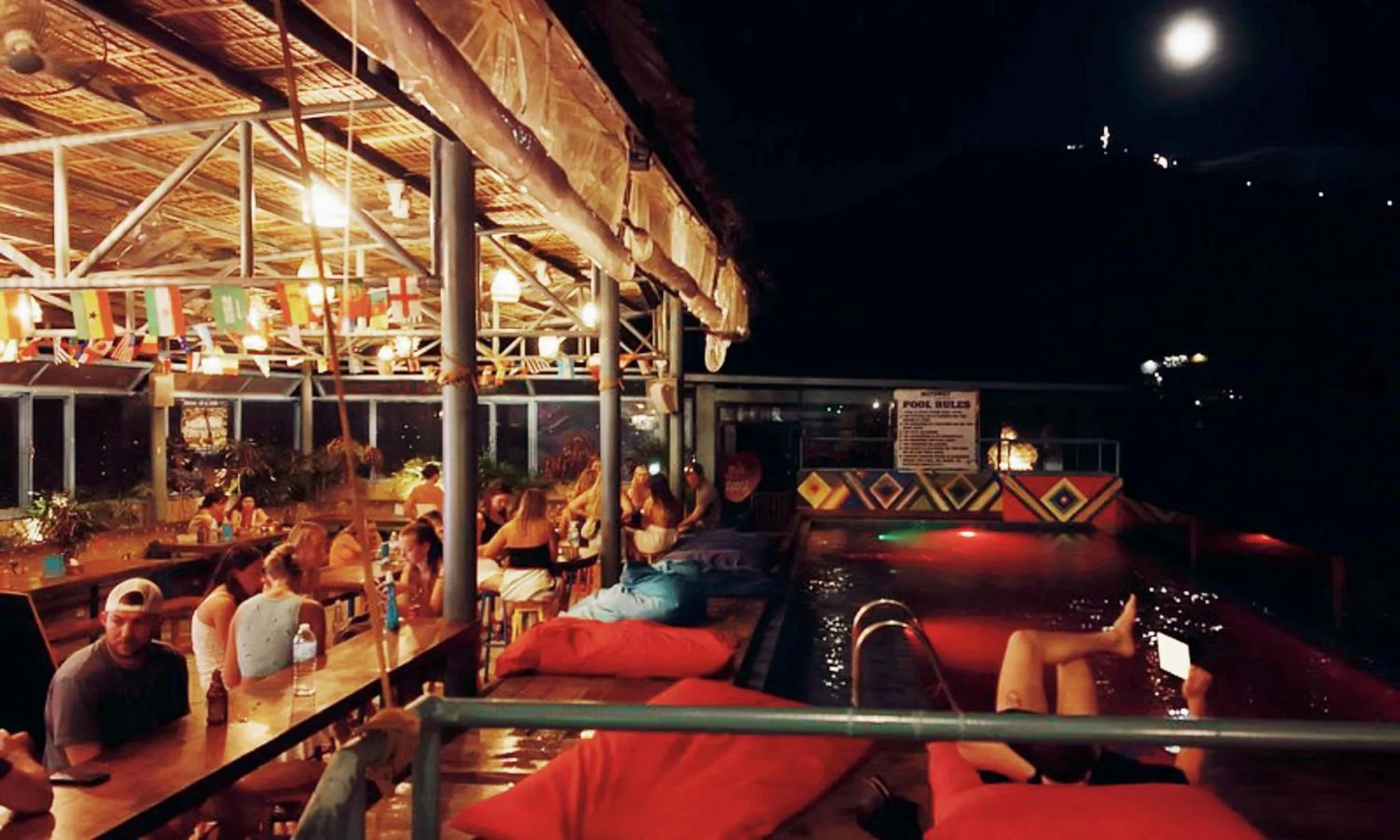 Une terrasse éclairée avec des clients assis autour d'un bar et de tables basses.