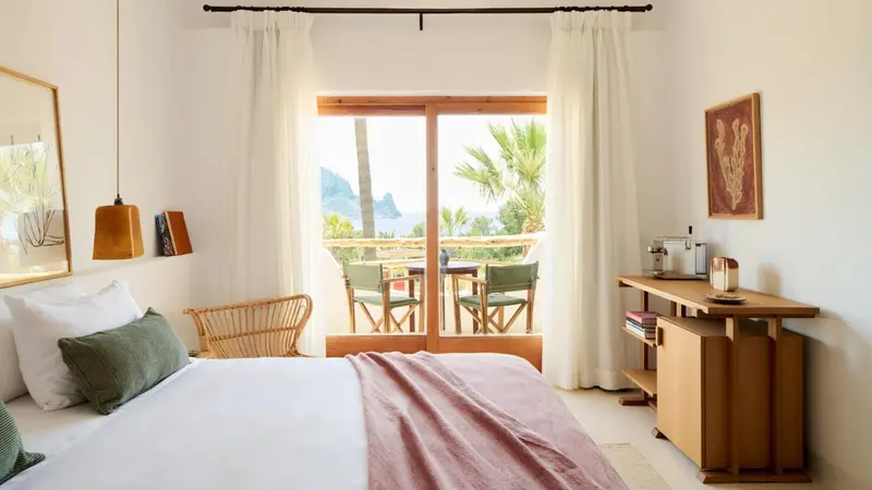Chambre lumineuse avec un lit et une vue sur la mer depuis une terrasse.
