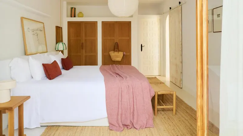 Une chambre lumineuse avec un grand lit recouvert de linge blanc et de coussins colorés.