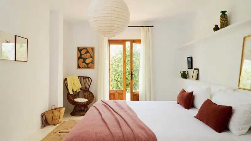 Une chambre lumineuse avec un lit fait et une fenêtre ouverte sur la végétation.