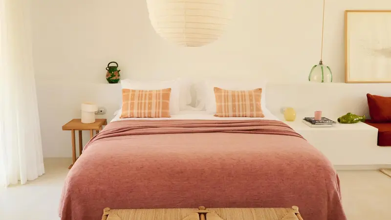 Un lit double avec des oreillers et une couverture rose dans une chambre lumineuse.