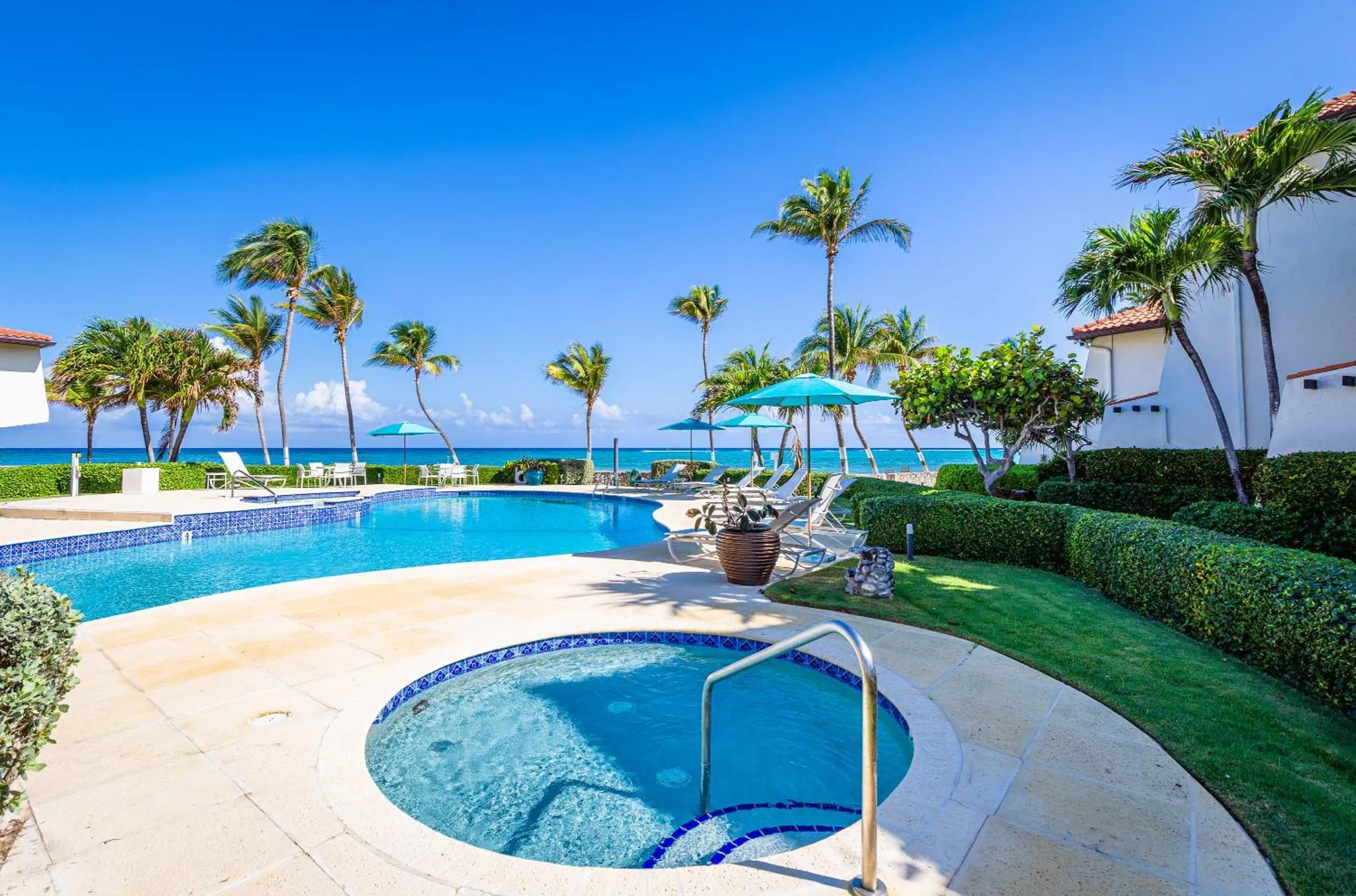 Piscine et jacuzzi avec transats et végétation tropicale face à la mer.