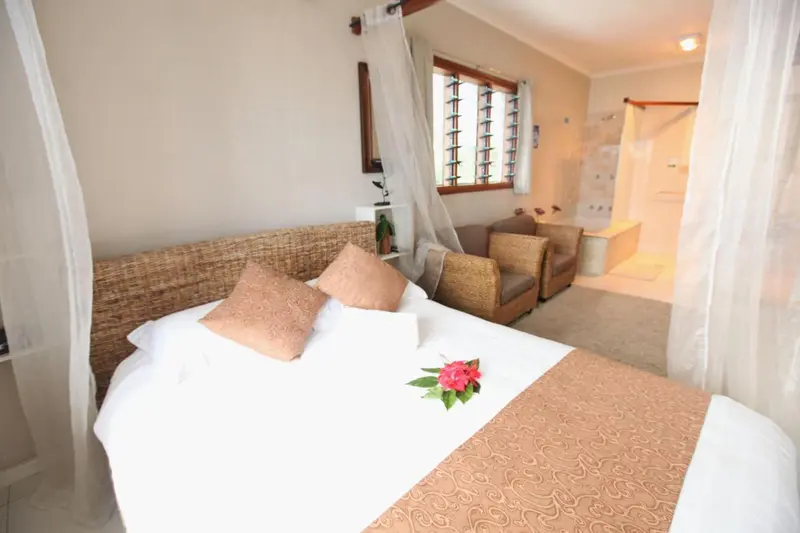 Une chambre lumineuse avec un lit recouvert de moustiquaire et un coin salon.