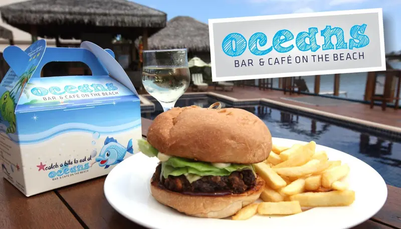 Un hamburger avec des frites et une boisson servis sur une table en extérieur.