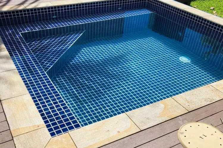 Petite piscine carree aux carreaux bleus et blancs, avec un espace de repos en bois.