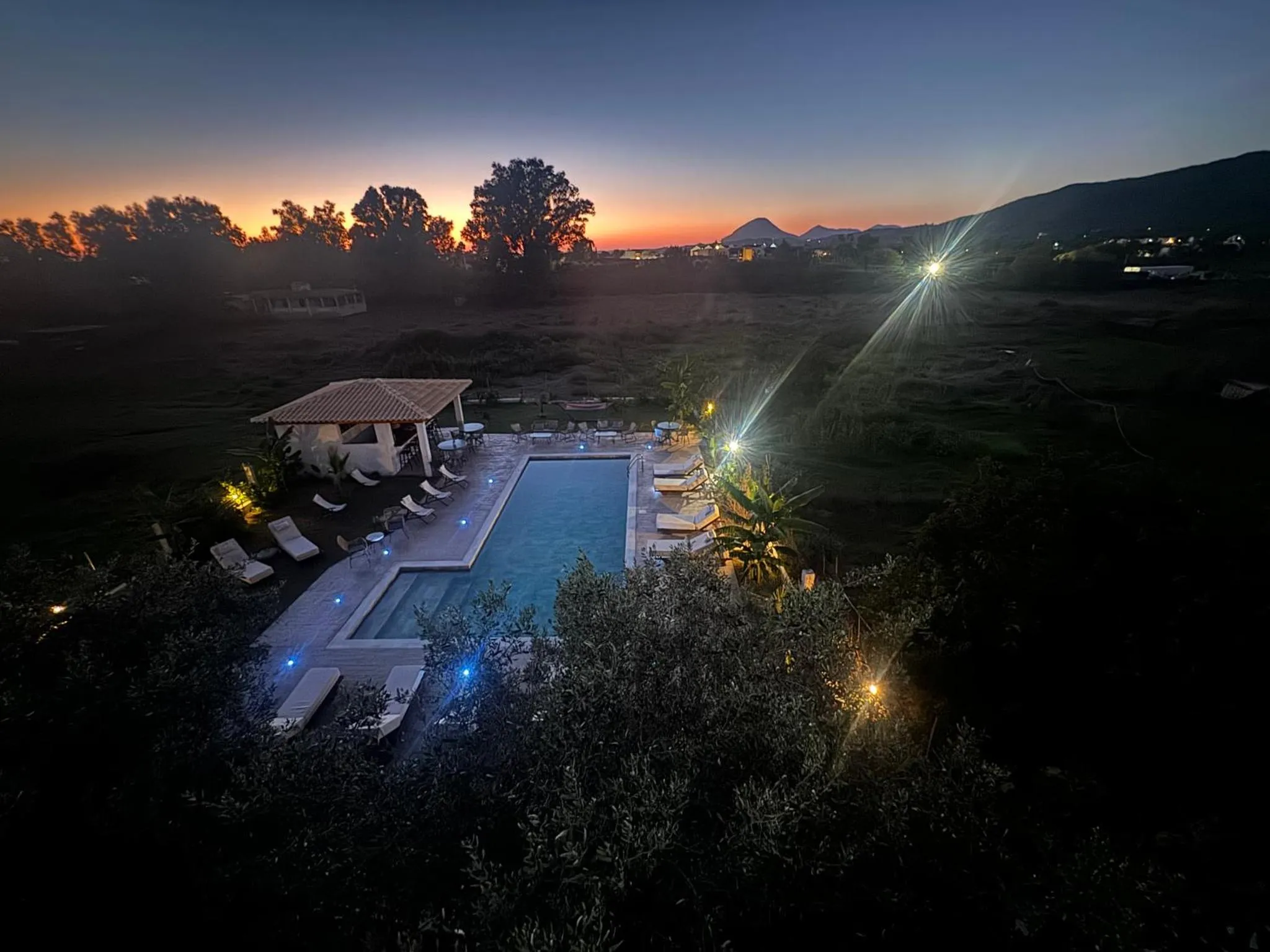 Piscine extérieure illuminée avec transats et végétation luxuriante au crépuscule.