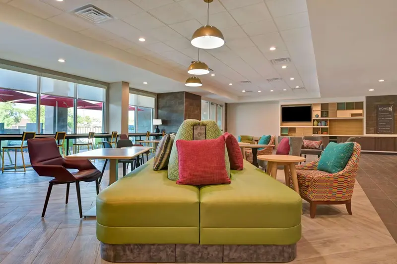 Espace de détente avec canapés verts et fauteuils colorés près de grandes fenêtres.