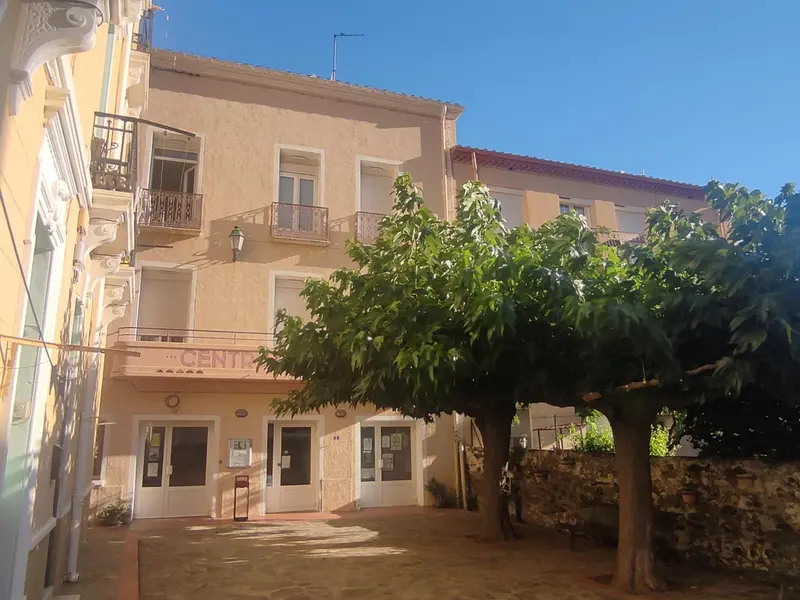 Façade d'un bâtiment beige à deux étages avec des ouvertures et un arbre devant.
