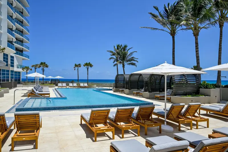 Une piscine bordée de transats blancs sous des parasols, avec une vue sur la mer.