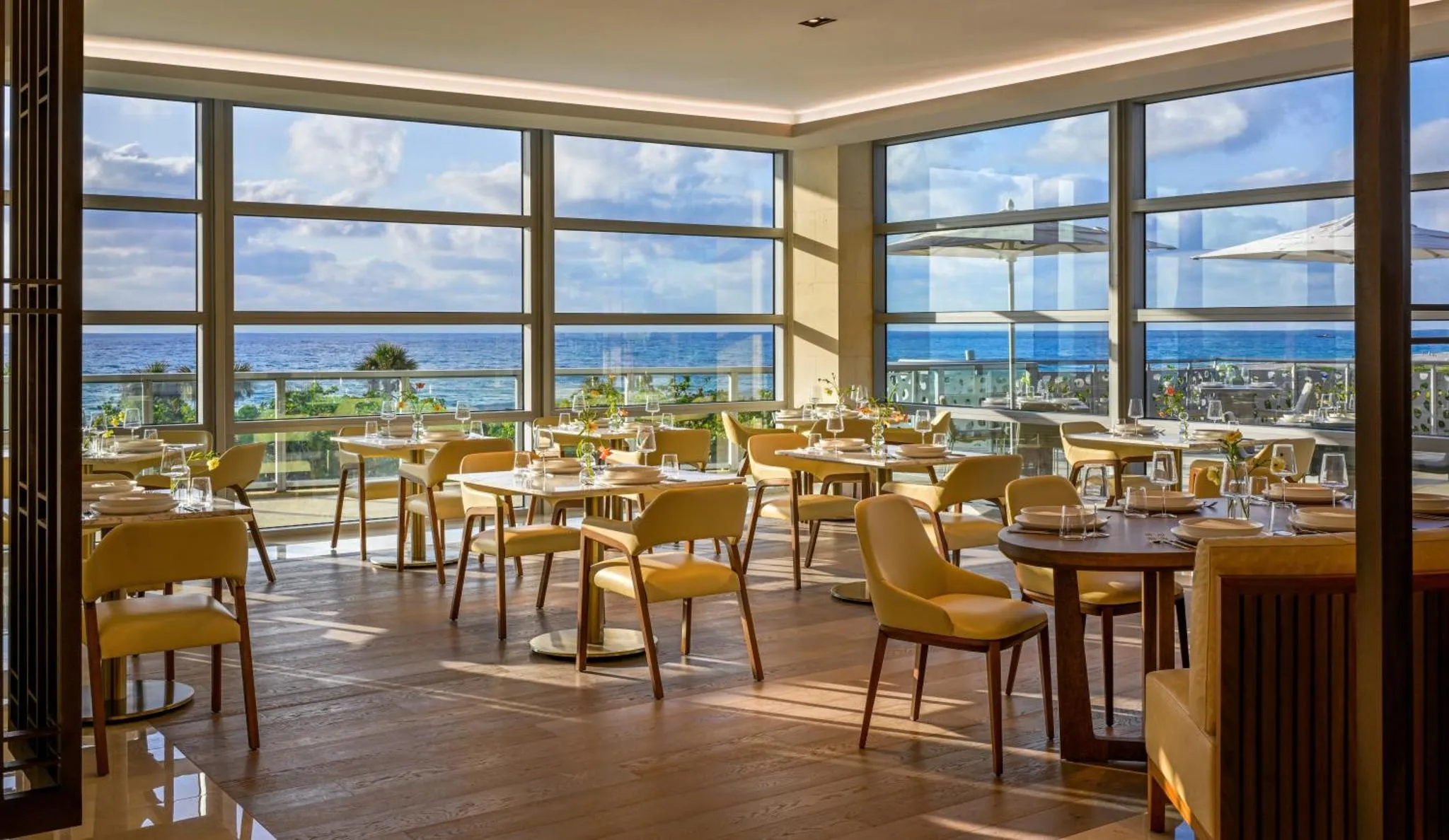 Une salle lumineuse avec des tables dressées face à une vue sur la mer.