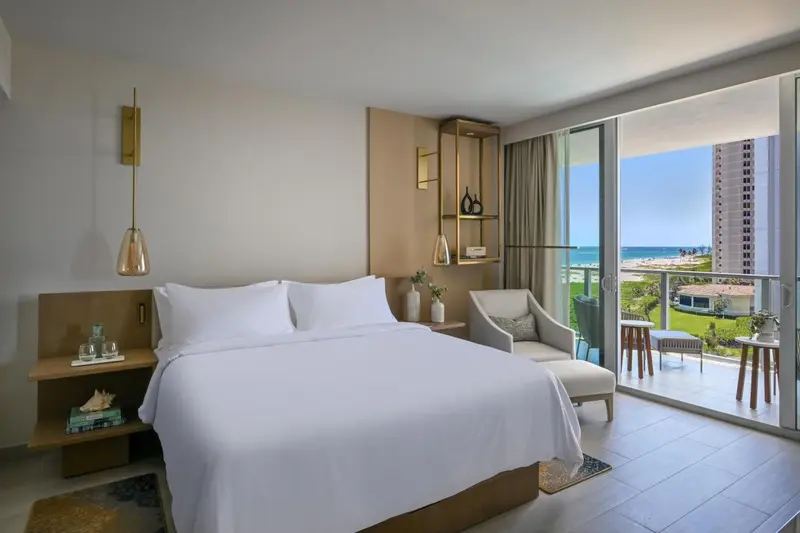Chambre lumineuse avec un grand lit et vue sur la mer depuis un balcon.