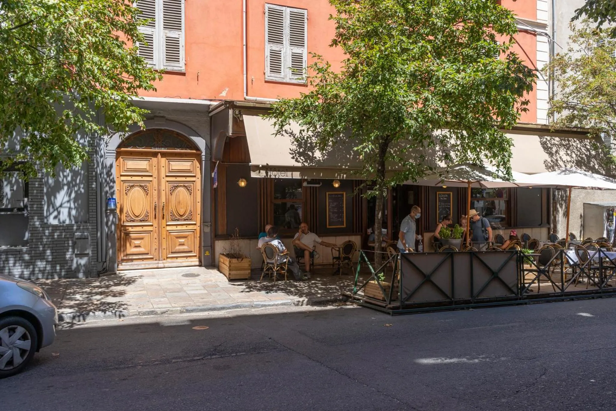 Terrasse de café en bord de rue avec des clients assis à des tables.