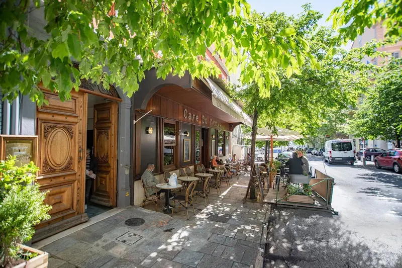 Terrasse de café ensoleillée avec tables et chaises en bord de rue.