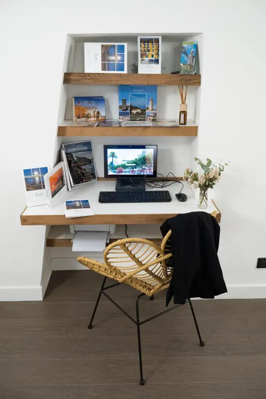 Un espace de travail avec un bureau, une chaise en rotin et des étagères décoratives.
