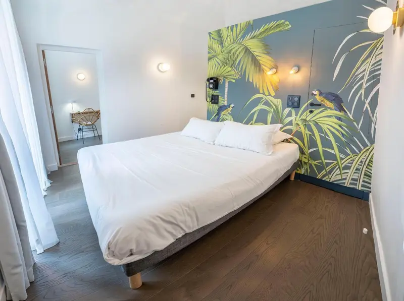 Une chambre lumineuse avec un grand lit et un mur décoré de motifs tropicaux.