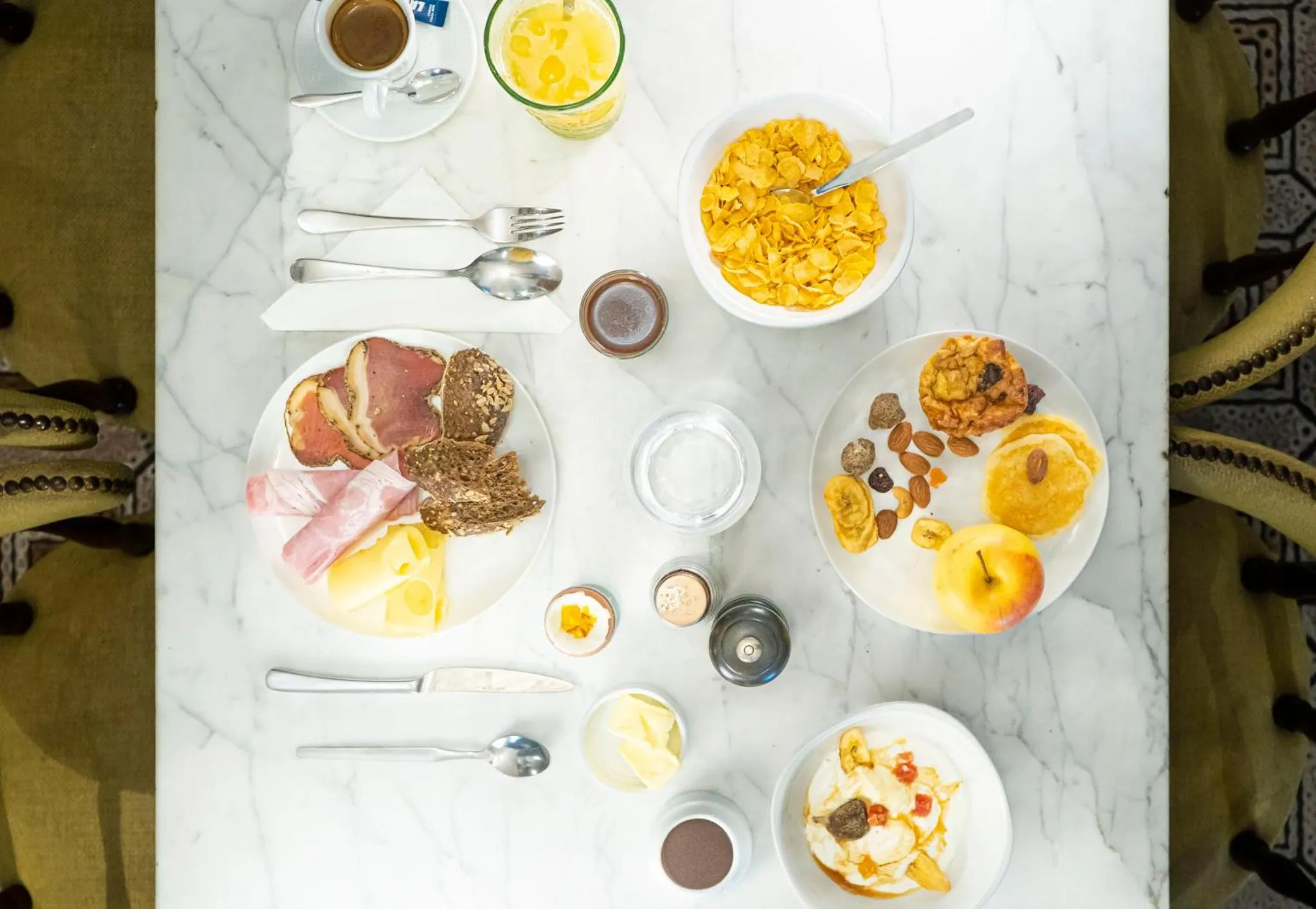 Une table est dressée avec un petit-déjeuner composé de viennoiseries, de charcuterie, de fruits et de céréales.