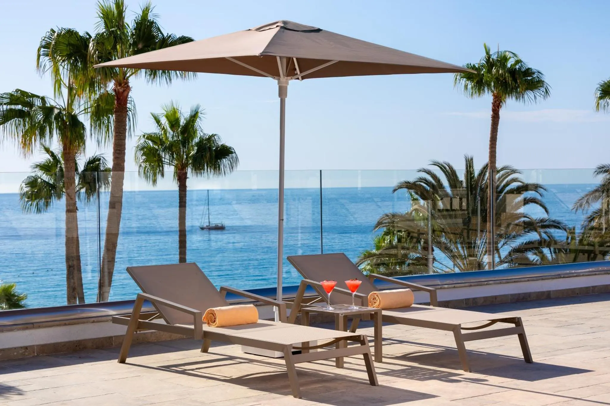 Deux transats avec des cocktails sont posés sur une terrasse ensoleillée avec vue sur la mer.