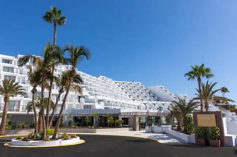Façade blanche d'un bâtiment moderne bordée de palmiers sous un ciel bleu.
