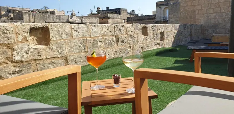 Deux verres de cocktails colorés sur une petite table en bois, devant des fauteuils sur une terrasse.
