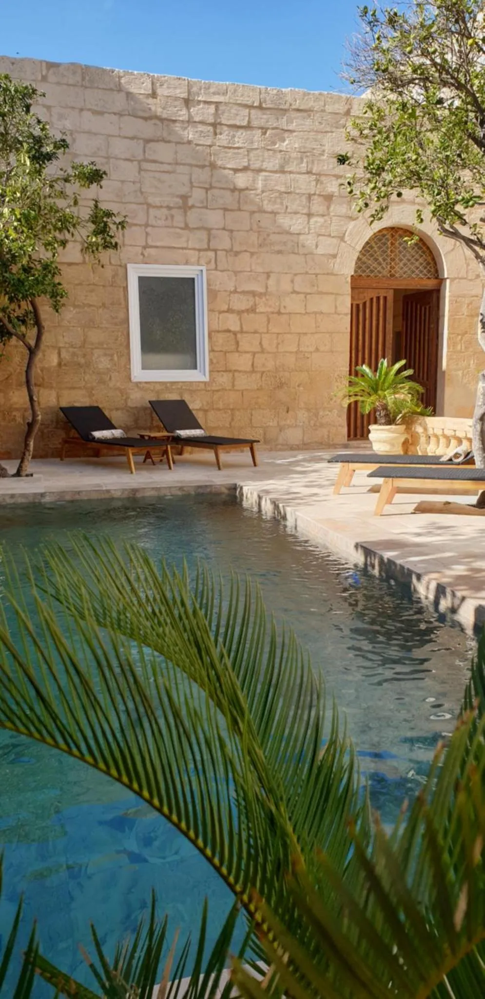 Deux transats sont installés au bord d'une piscine dans une cour ombragée.