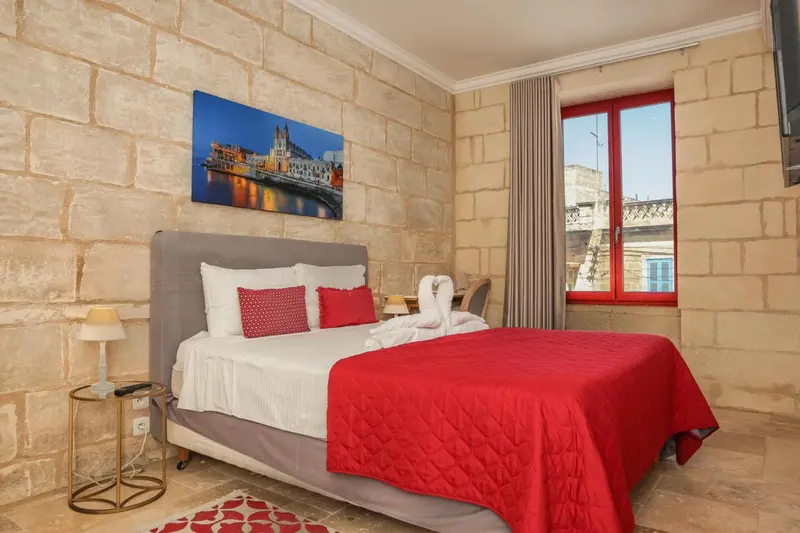 Une chambre lumineuse avec un grand lit recouvert d'une couverture rouge et un tableau au mur.