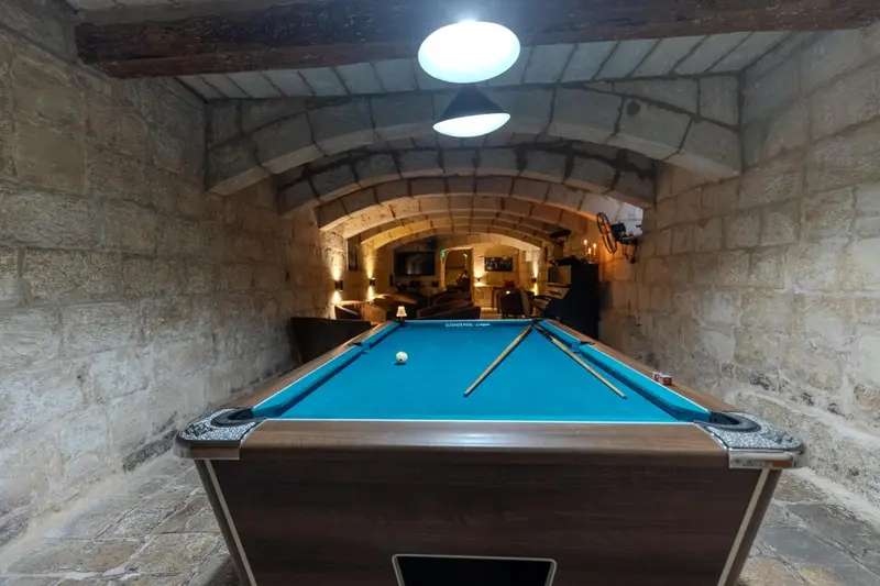 Une table de billard en bois se trouve dans une pièce voûtée éclairée par des spots.