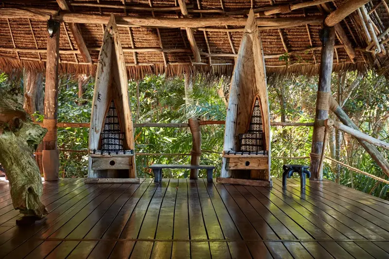 Terrasse en bois abritée par un toit de chaume, avec des rangées de combinaisons de plongée.