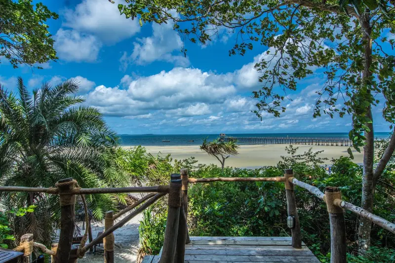 Vue sur une plage de sable blanc et une mer turquoise sous un ciel nuageux.
