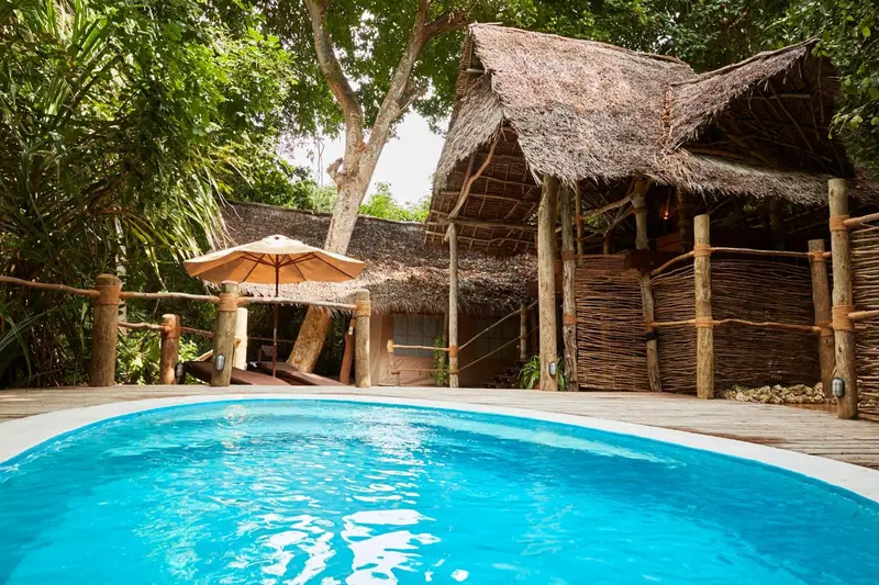 Une petite piscine turquoise est devant une structure en bois et en chaume.