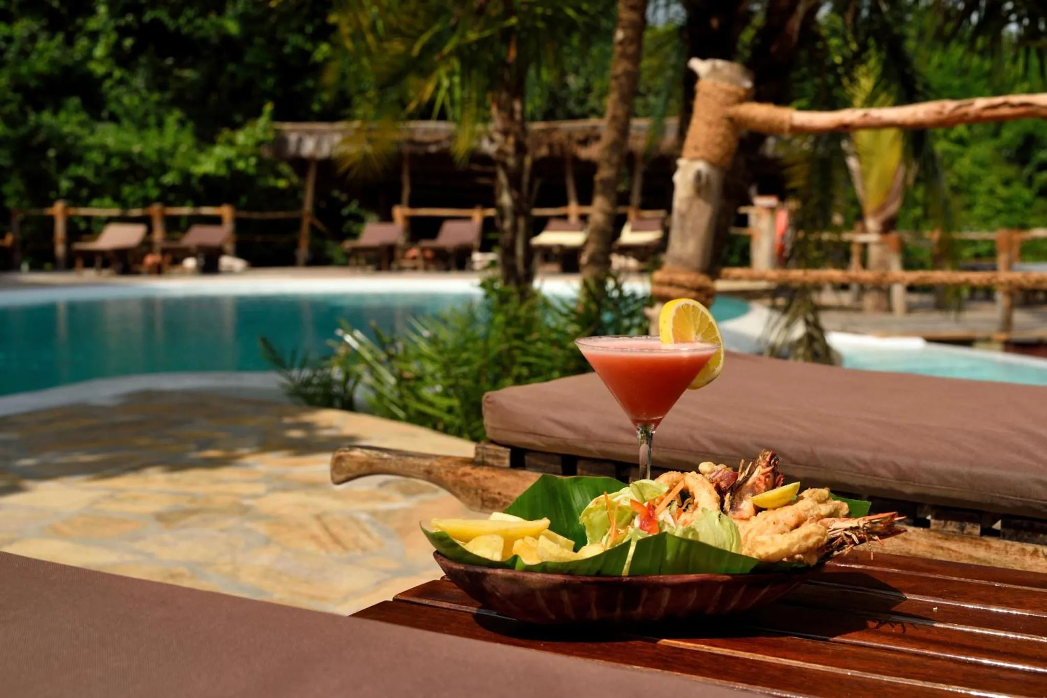 Un cocktail et une assiette de fruits de mer sont servis au bord d'une piscine.