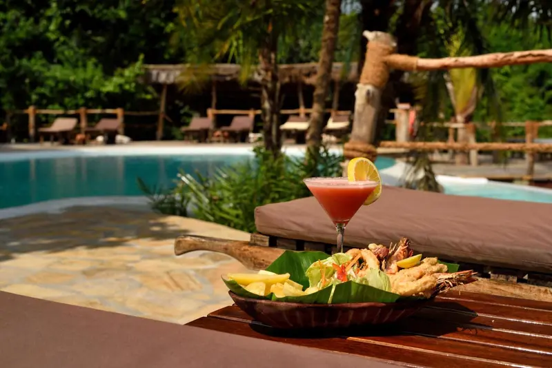 Un cocktail et une assiette de fruits de mer sont servis au bord d'une piscine.