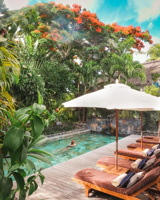 Transats et parasols bordent une piscine turquoise dans un jardin tropical luxuriant.