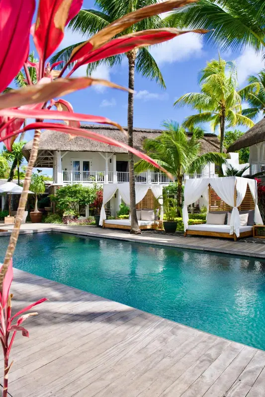 Une piscine turquoise bordée d'une terrasse avec des lits balinais et une végétation luxuriante.