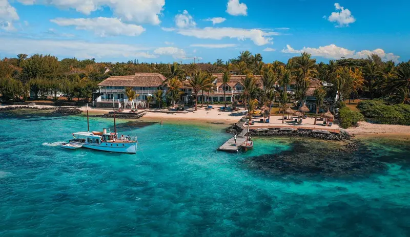 Vue aérienne d'un établissement balnéaire avec un bateau amarré dans une baie turquoise.