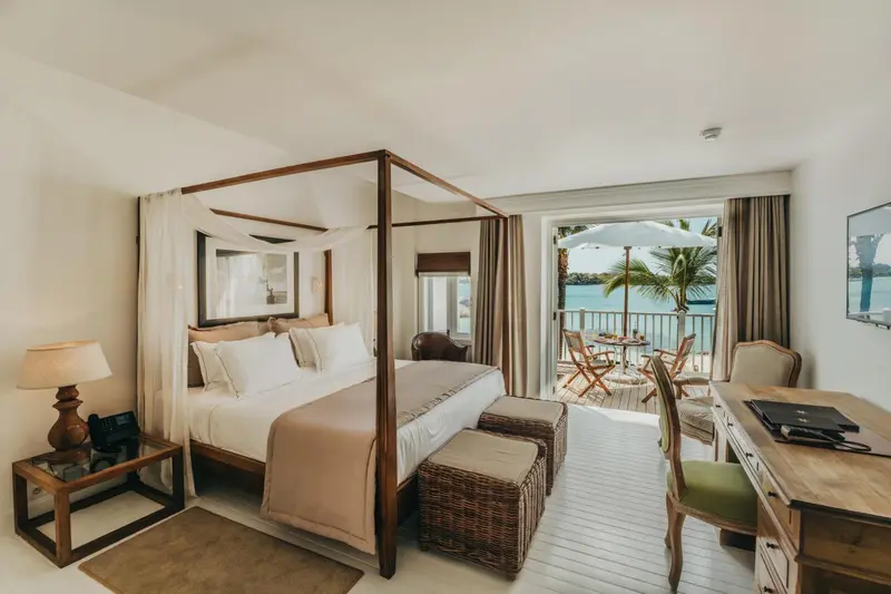Une chambre lumineuse avec un grand lit à baldaquin donnant sur une terrasse et la mer.