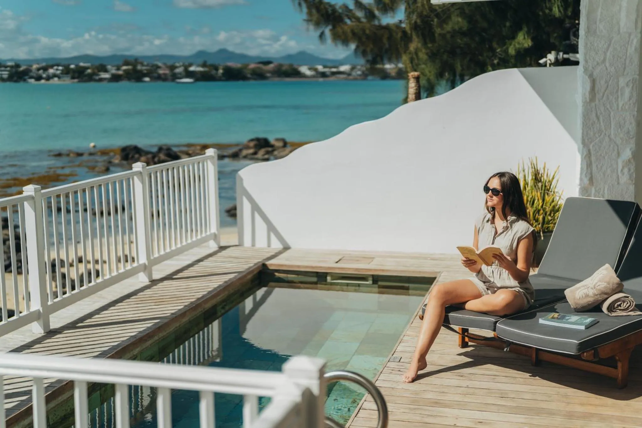 Une femme lit un livre au bord d'une piscine sur une terrasse.