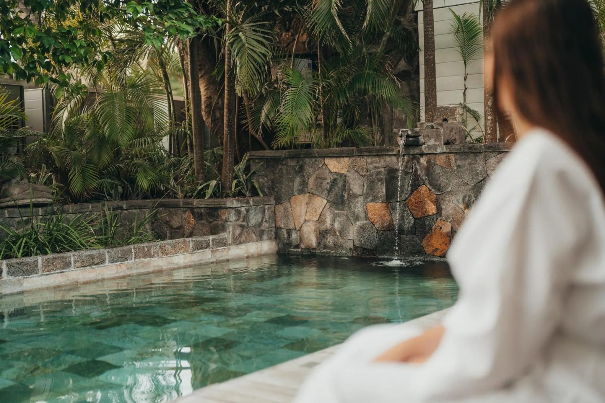 Une personne contemple un jardin tropical depuis le bord d'une piscine.