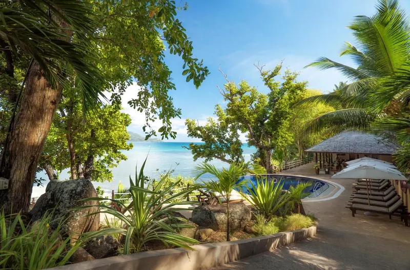 Une piscine bordée de végétation tropicale surplombe une plage de sable blanc.