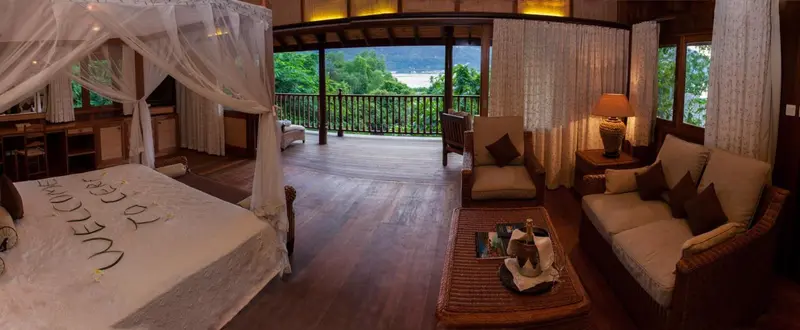 Une chambre spacieuse s'ouvre sur une terrasse en bois avec vue sur la végétation.