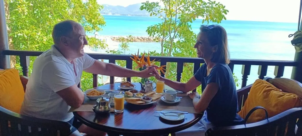Un couple prend son petit-déjeuner sur une terrasse ensoleillée avec vue sur la mer.