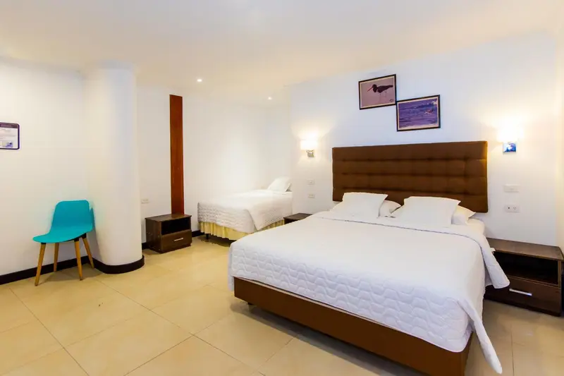 Une chambre lumineuse avec deux lits et une chaise turquoise.