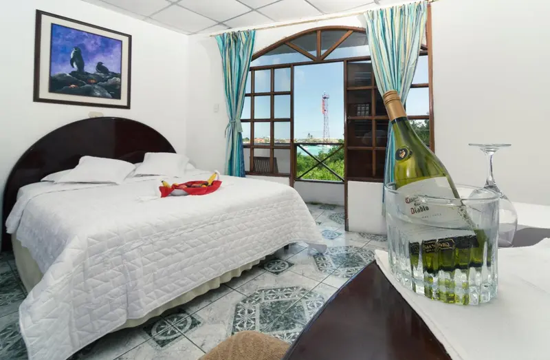 Une chambre lumineuse avec un lit blanc et une bouteille de vin sur une table.