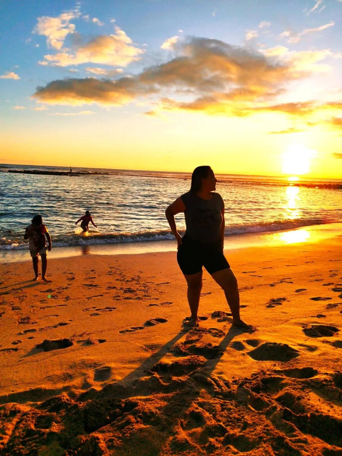 Personne se tenant sur une plage de sable au coucher du soleil.