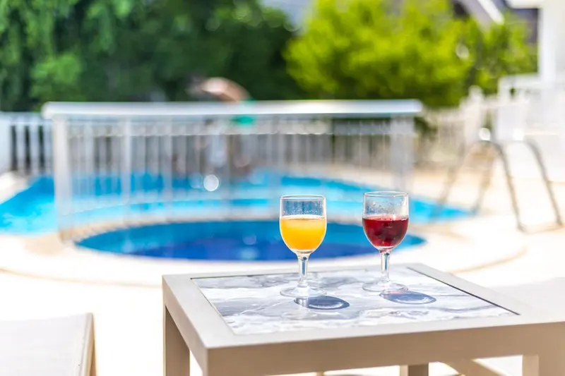 Deux verres de boissons colorées sur une table basse au bord d'une piscine.