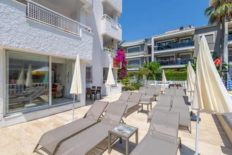 Terrasse avec transats et parasols devant un bâtiment blanc.