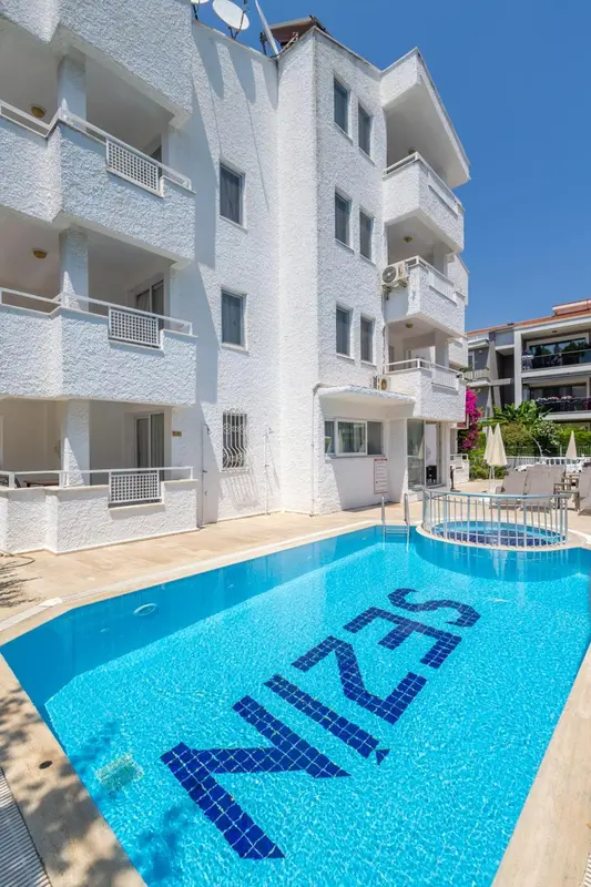 Bâtiment blanc avec des balcons surplombant une piscine bleue.