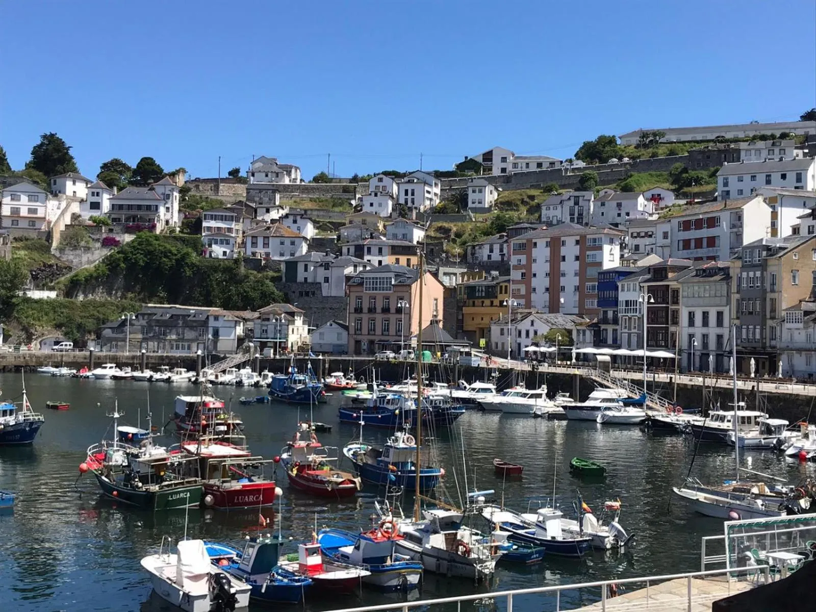 Vue d'un port de plaisance avec des bateaux amarrés et des maisons colorées sur les collines.